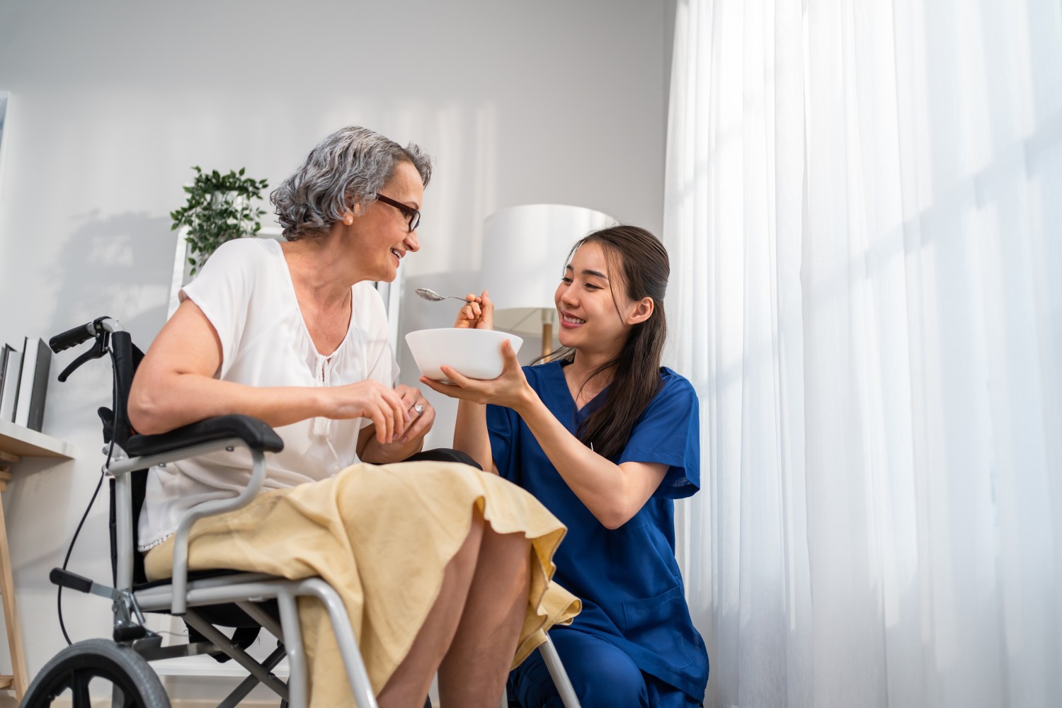 A caregiver providing attentive personal care assistance to an elderly woman in a wheelchair at home