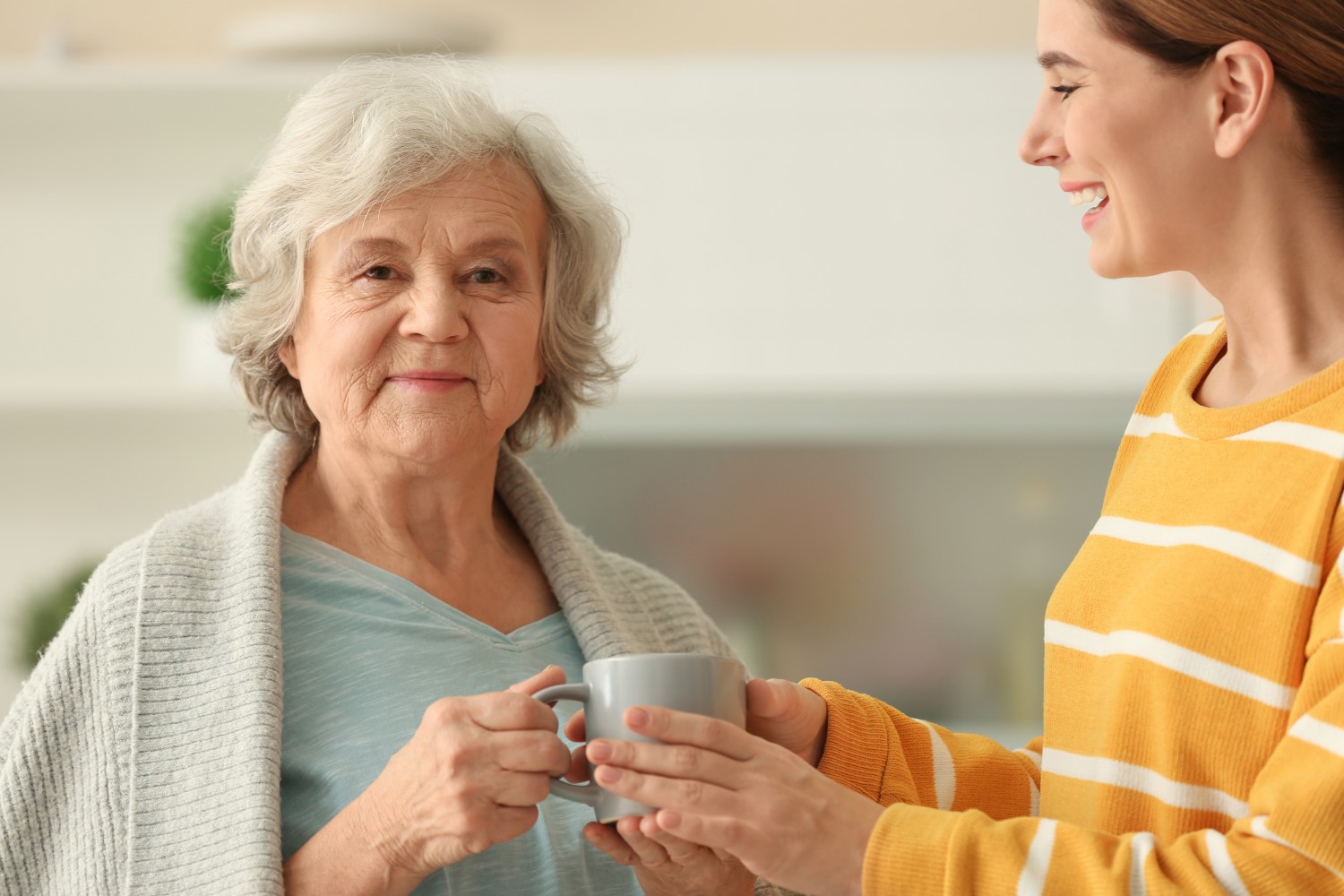 A caregiver offering a warm cup of tea to an elderly woman, representing attentive homemaker care