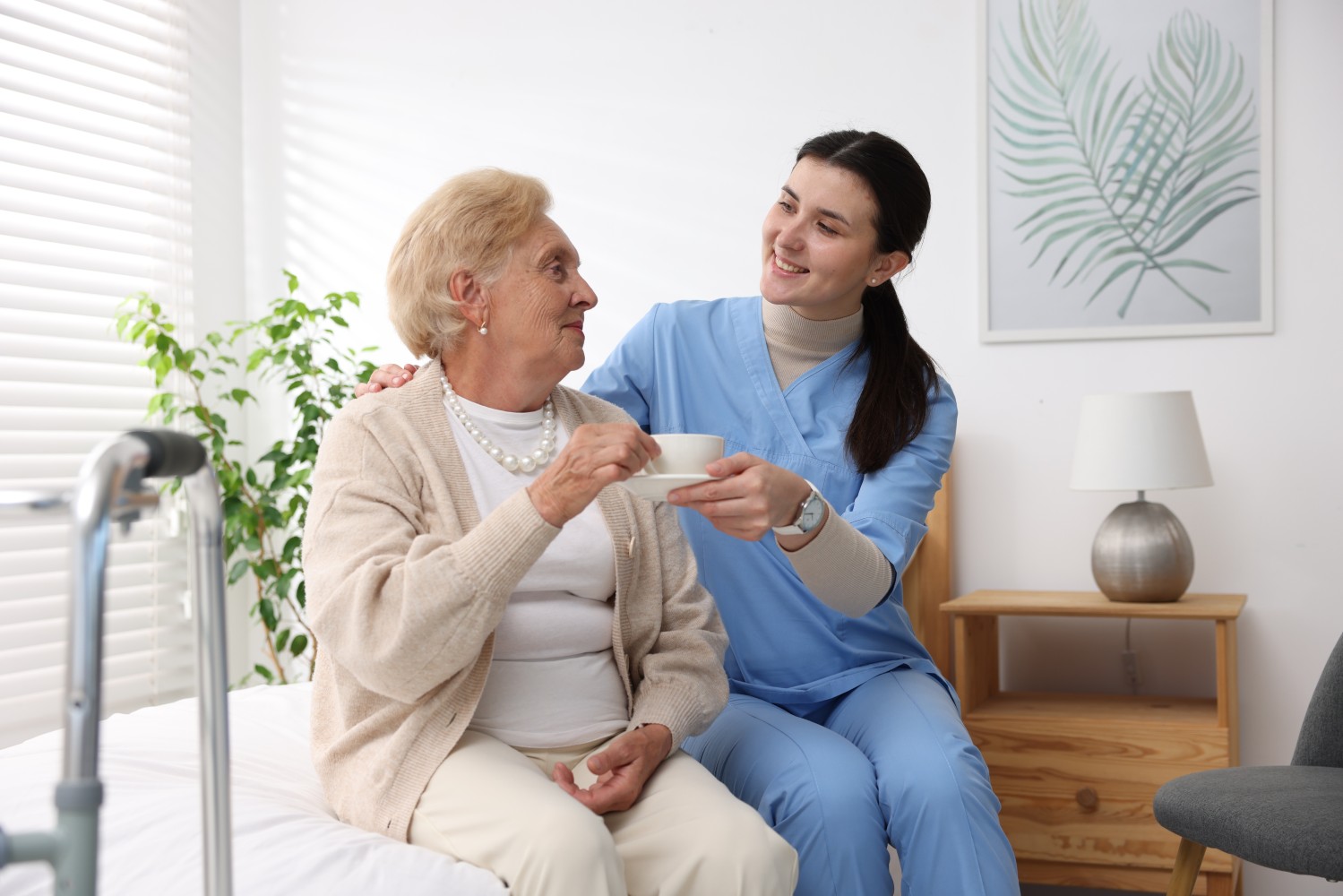 A caregiver serving a warm cup of tea to a smiling senior woman, representing homemaker care
