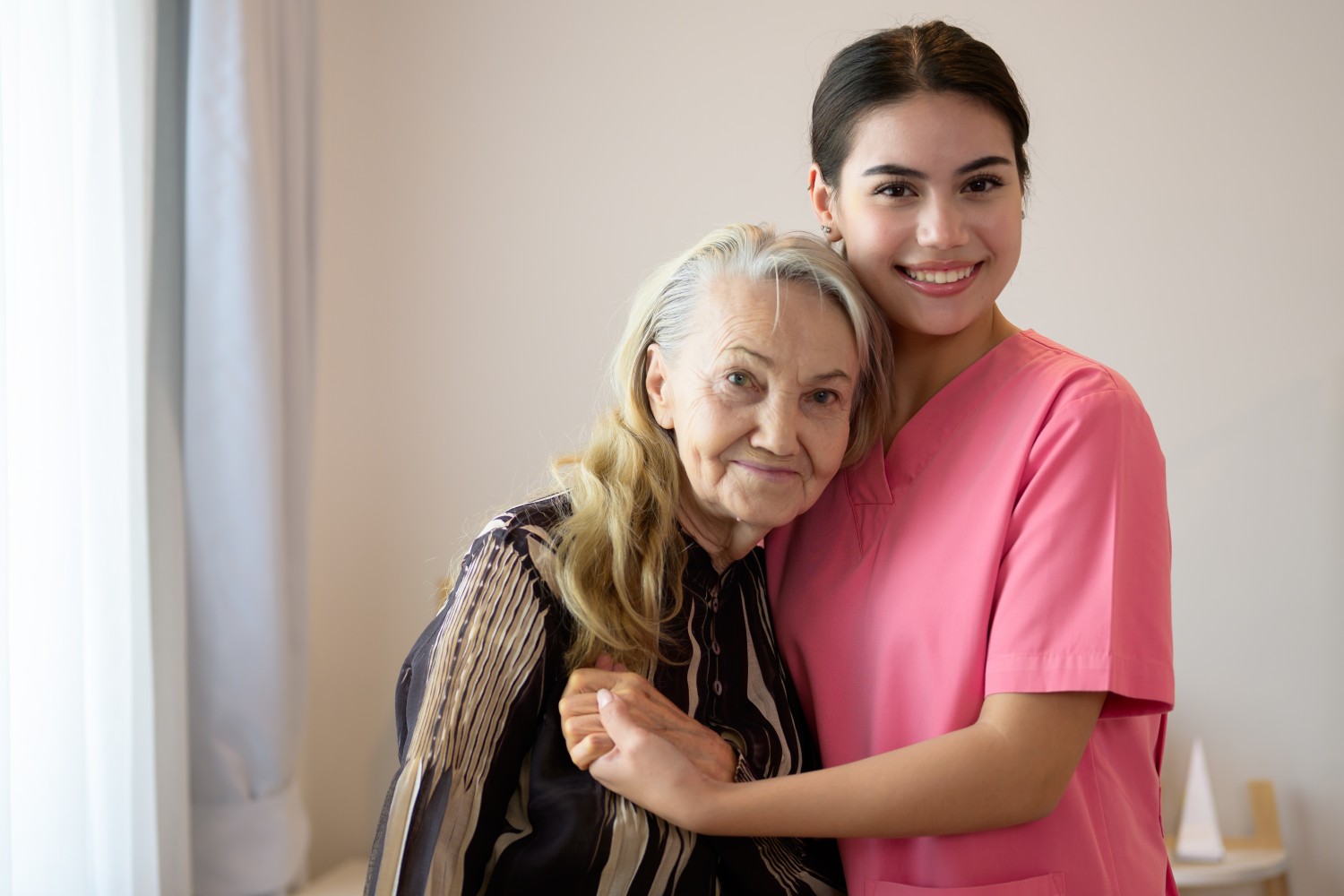 A caregiver warmly embracing an elderly woman in a home setting